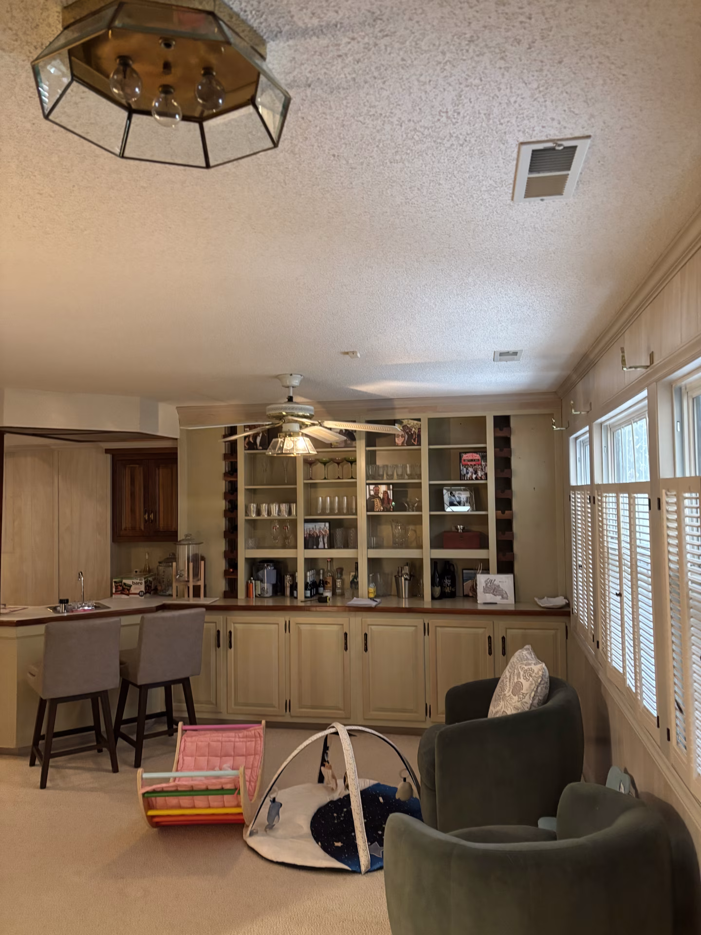 Before the renovation: carpeted room with light-colored lower cabinets, a wall of shelving, and shuttered windows.