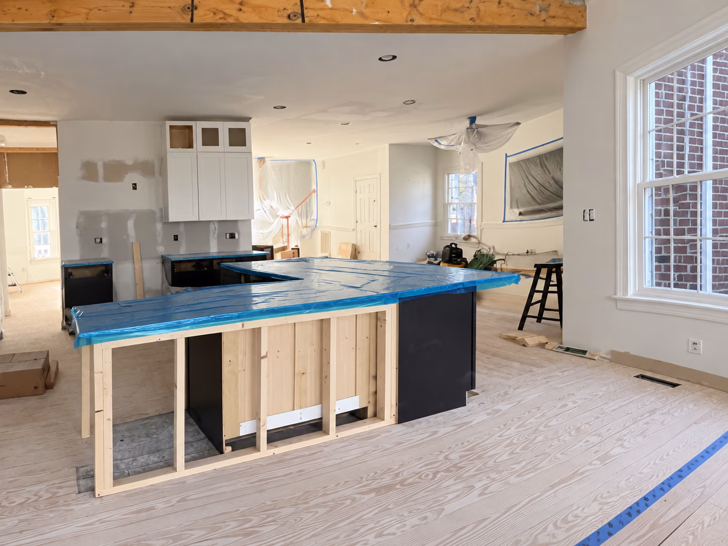 Kitchen during construction showing counter protection, exposed framing and drywall preparation.