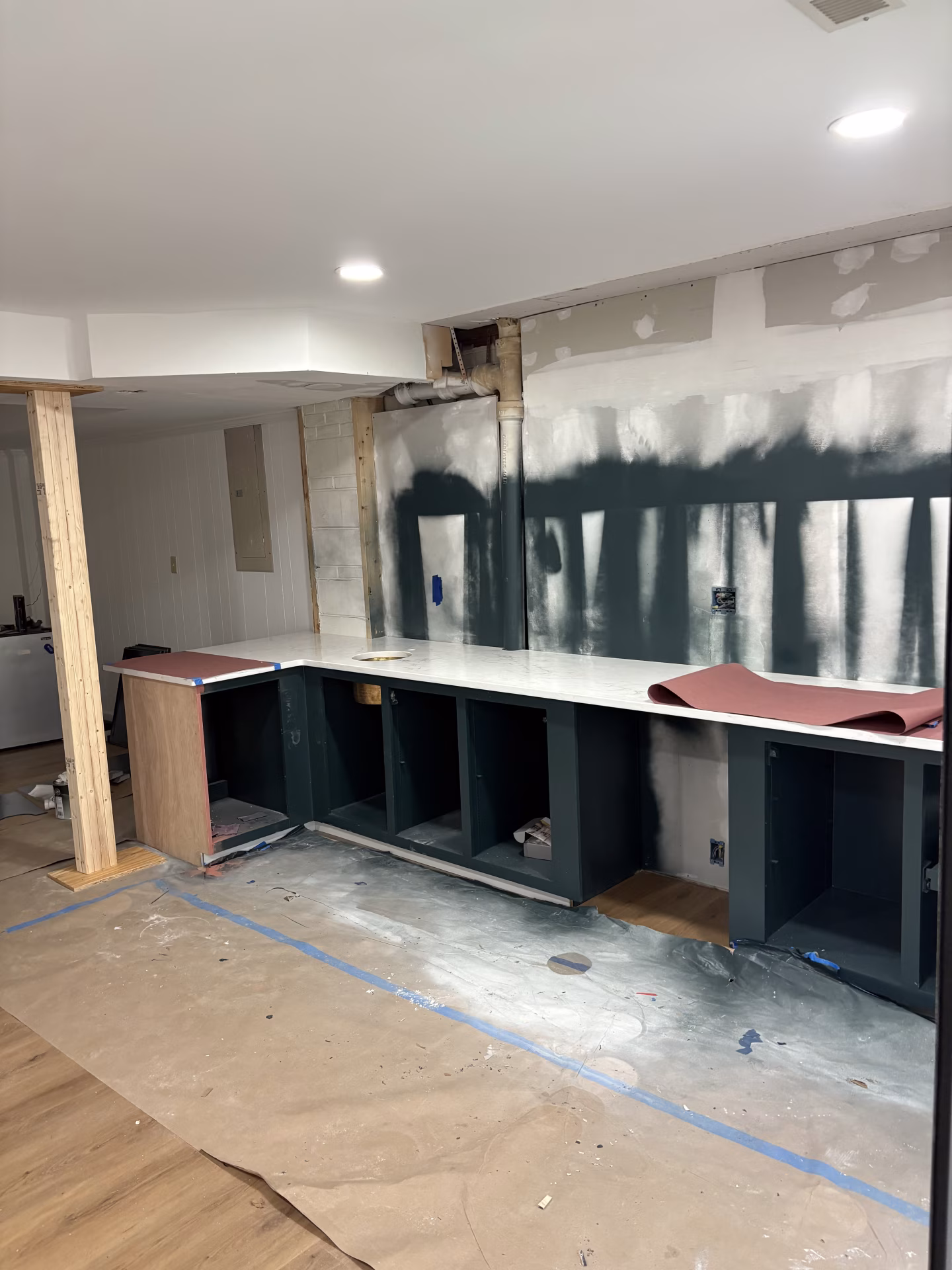 Bar renovation in progress, showing removed upper shelving, dark-painted lower cabinet frames, and wall preparation.